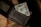 A textured black wallet partially open with a one-dollar bill protruding from one of the compartments. The wallet is placed on a surface that seems to be wooden and has a coarse woven mat beneath it.