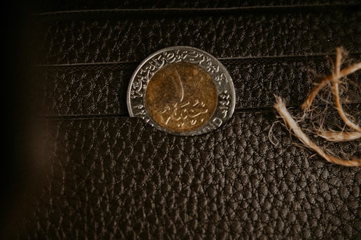 A coin with intricate, possibly Arabic script, is placed on a textured dark brown leather surface. To the right, a coarse piece of string is visible.