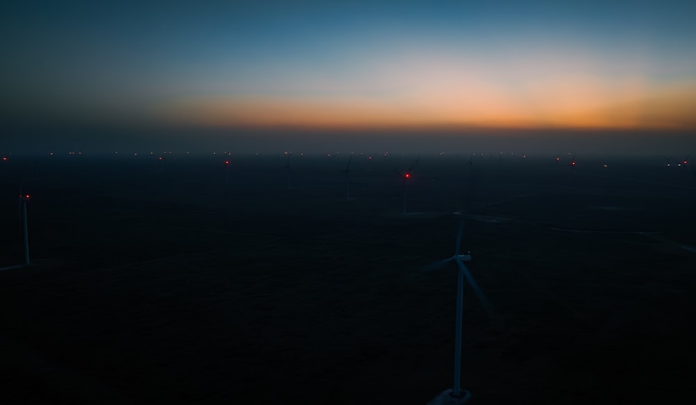 the sun is setting over a field of wind mills