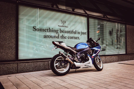 A sleek Suzuki motorcycle parked in front of the ruedaviva dealership on a sunny day.