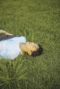 a young boy laying in the grass with his eyes closed