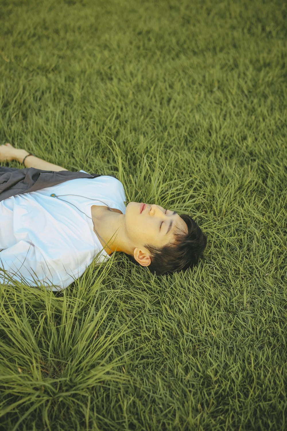 a young boy laying in the grass with his eyes closed