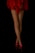 Fishnet stockings cover crossed legs, complemented by red high heels and a flowing red fabric skirt against a black background.