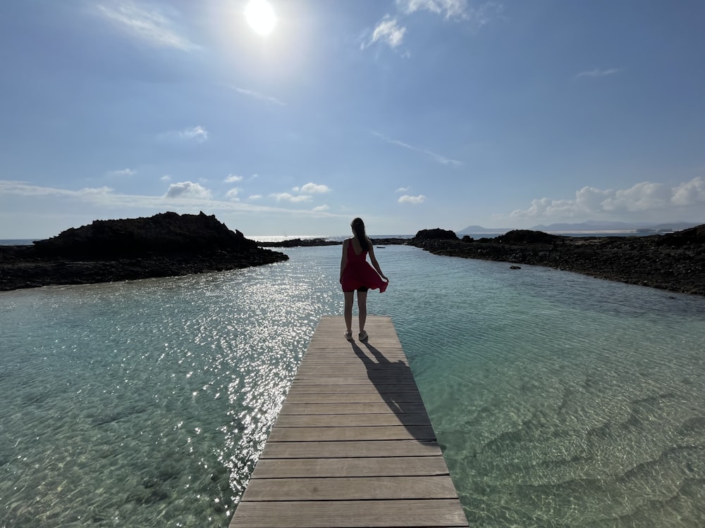 a woman in a red dress is walking on a dock