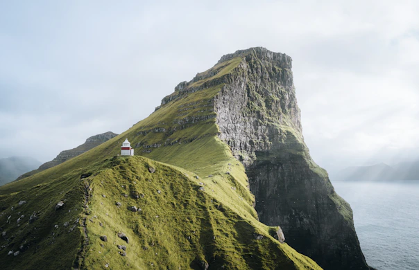 A small red and white lighthouse on a grassy cliff above the ocean