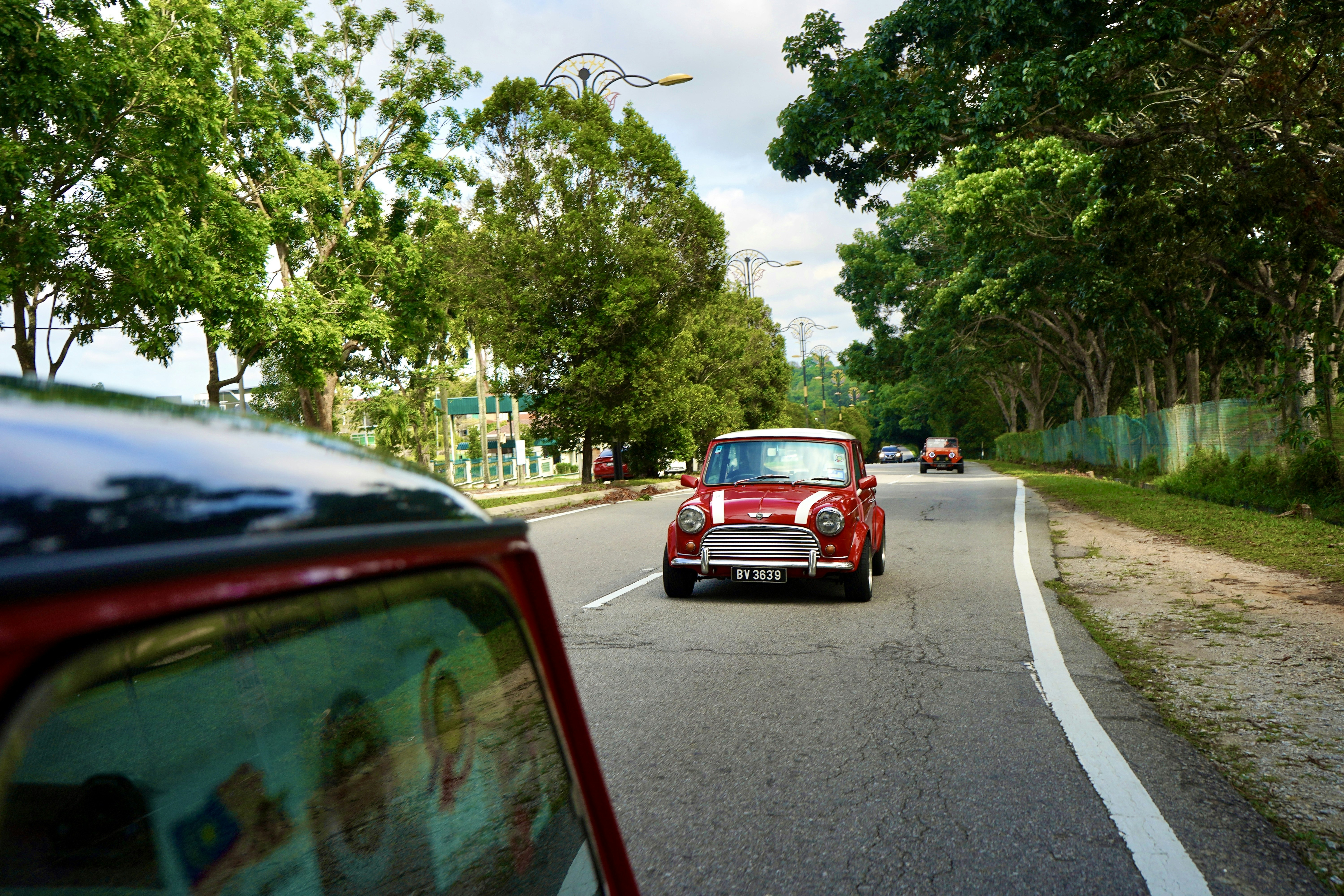 a red car driving down a street next to a lush green forest