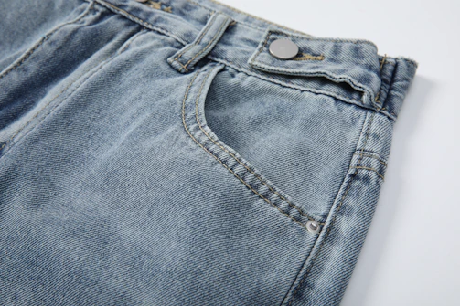 A stylish pair of denim jeans laid out on a rustic table with stitching details clearly visible.
