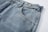 Close-up of a pair of blue denim jeans highlighting the texture and stitching. The focus is on the waistband, button, and a front pocket. The fabric appears sturdy with a slightly faded look.