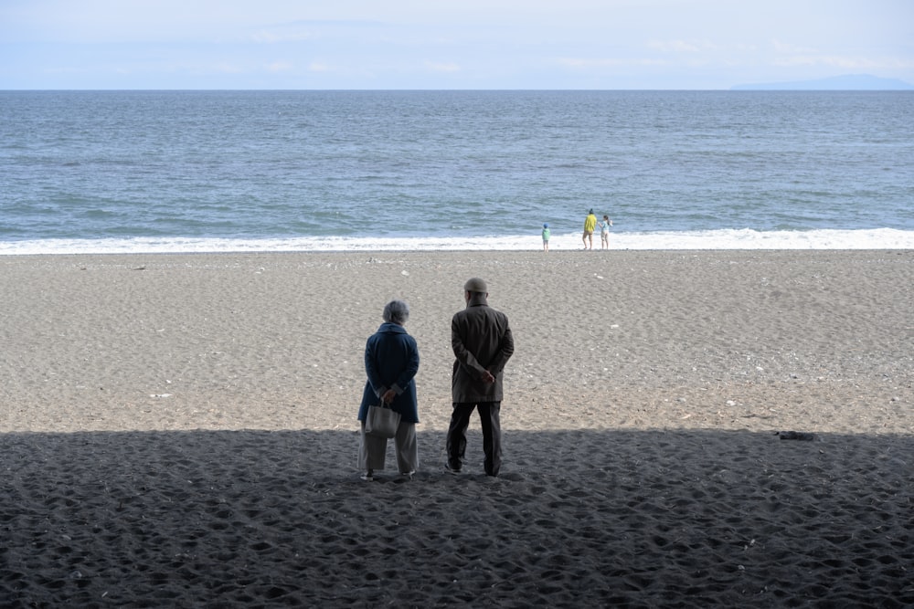 a couple of people standing on top of a sandy beach