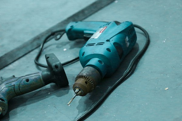 Máy khoan điện thân xanh có dây nguồn nằm trên nền bê tông xám