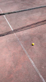 A tennis racket hitting a bright yellow ball mid-air on a clay court.