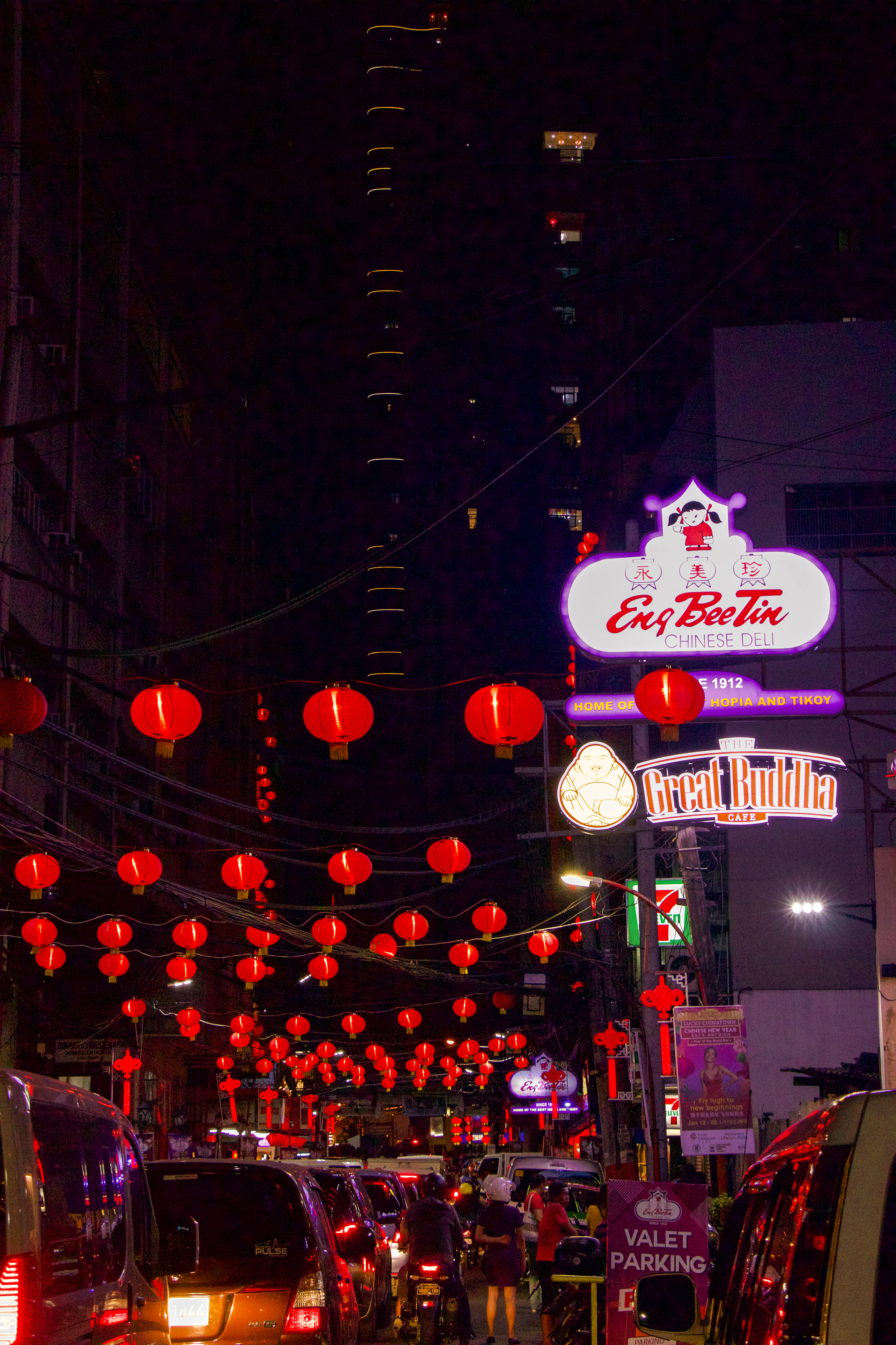 Red lanterns strung above a street in Binondo, Manila, neon shop signs glowing along the Chinatown block