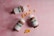 Three brown pill bottles with white caps, each labeled with green and white text, are scattered on a pink textured surface. Between the bottles, several small, round, yellow tablets are arranged in clusters.