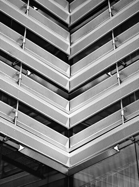 Angular architectural structure with repeating metallic patterns. The design features perforated metal sheets and linear elements, creating a modern and industrial aesthetic.