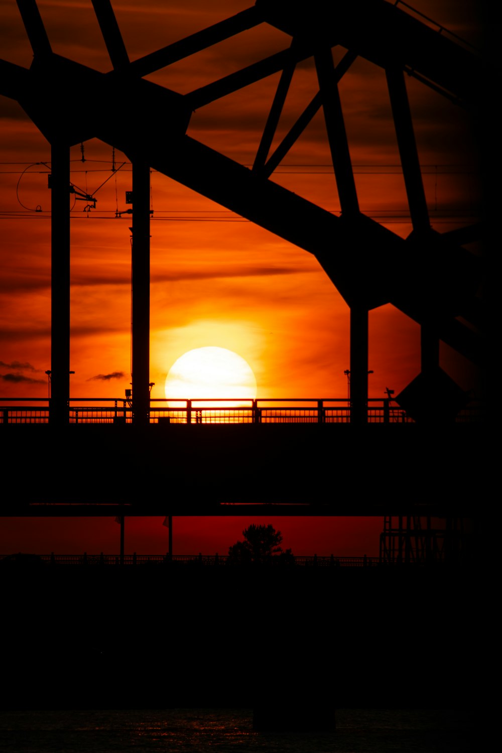 the sun is setting over a bridge over water