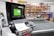 A computerized workstation in a workshop, featuring a monitor displaying green digital patterns and a keyboard and mouse in the foreground. Behind the workstation, there are shelves filled with various tools and materials, including rolls of fabric or paper.