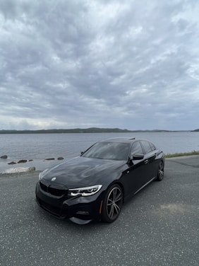 A sleek black luxury car shining under the sun near a coastal shoreline with gentle waves.