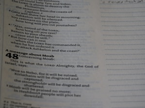 A close-up of a page from a religious text, possibly a Bible. The text discusses topics like the sword of the Lord and a message concerning Moab. The text is printed in two columns with a section heading in bold. It also includes chapter and verse numbers, with the number 48 prominently displayed.
