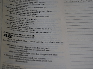 A close-up of a page from a religious text, possibly a Bible. The text discusses topics like the sword of the Lord and a message concerning Moab. The text is printed in two columns with a section heading in bold. It also includes chapter and verse numbers, with the number 48 prominently displayed.