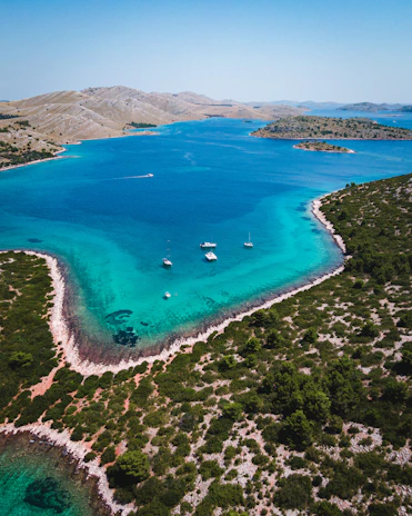 Aerial view of azure waters dotted with yachts anchored near pristine white sandy beaches.