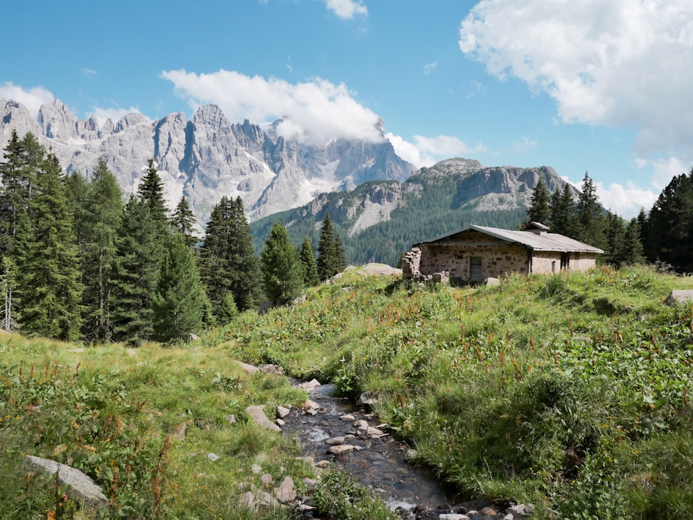 a small cabin in the mountains with a stream running through it