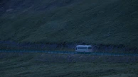 Medium-sized bus with 40 seats cruising along a highway surrounded by hills.