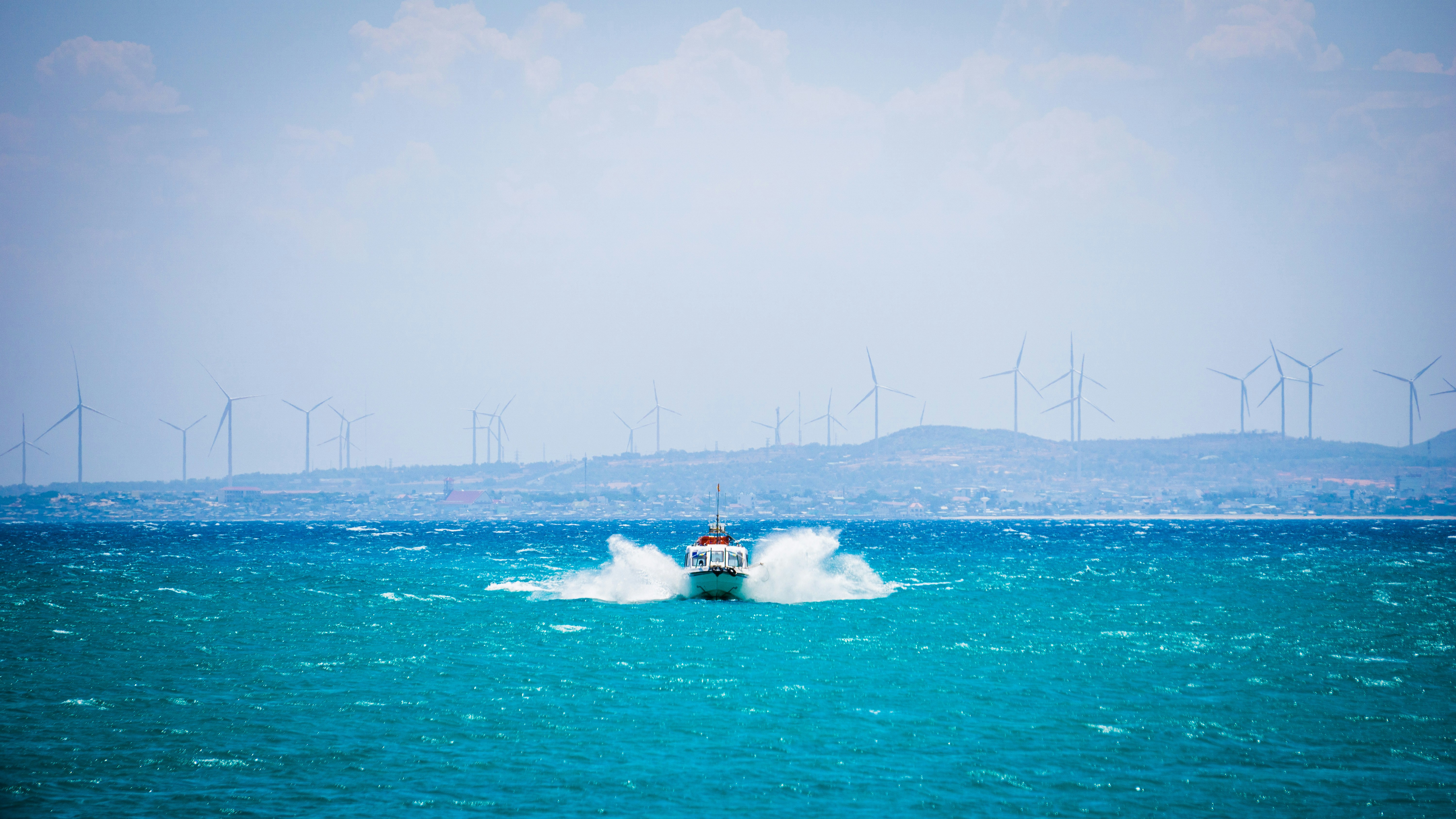 a boat in the middle of the ocean with wind mills in the background