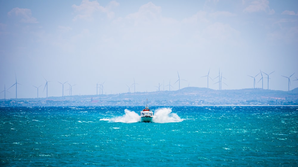 Um barco no meio do oceano com moinhos de vento ao fundo