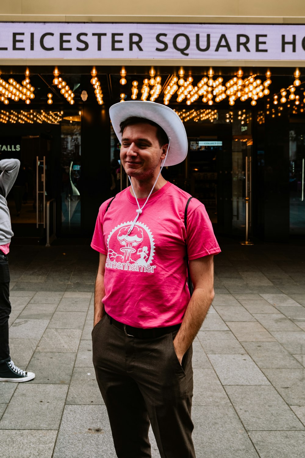 a man in a pink shirt and hat standing in front of a theater