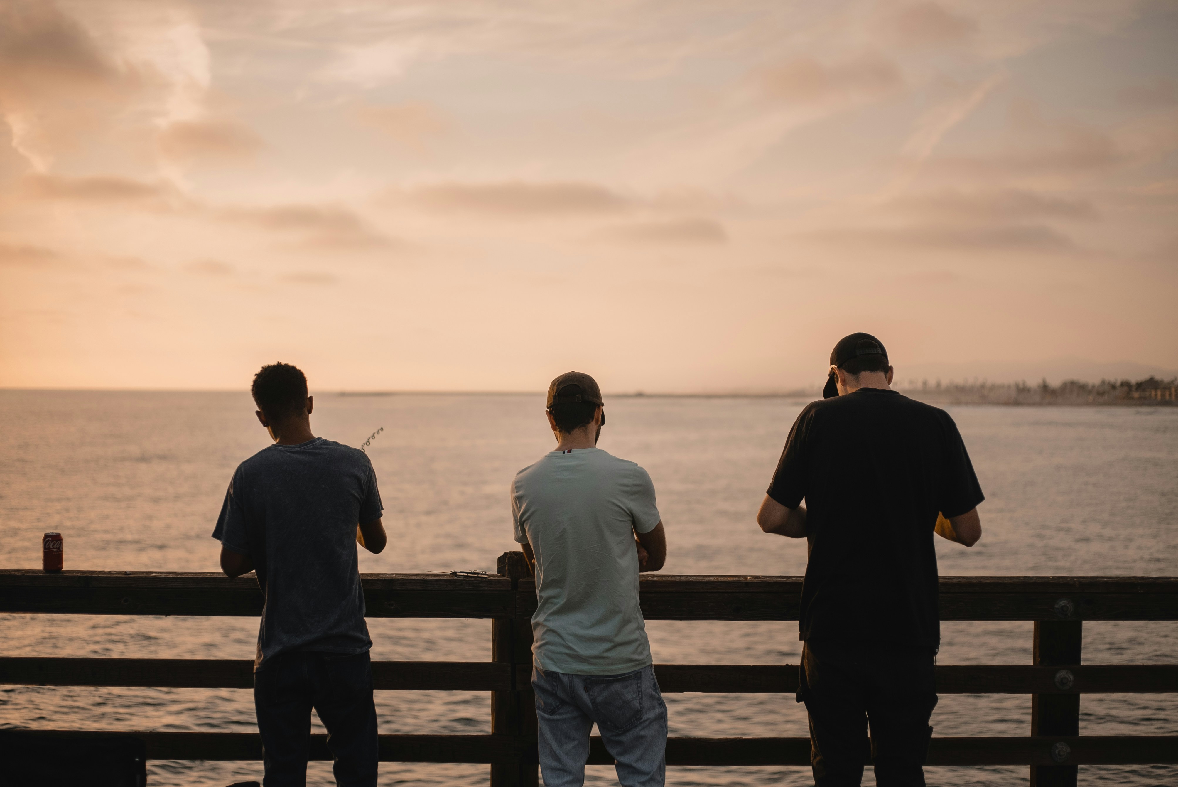 three men standing on a pier looking out at the water
