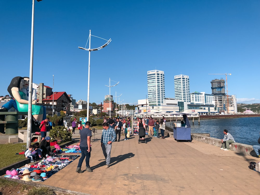 a group of people walking down a sidewalk next to a body of water