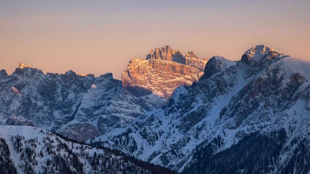 a mountain range covered in snow at sunset