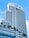 A tall modern hotel building with numerous windows and a sleek architectural design. The hotel name is visible at the top, and there are palm trees adorning the lower levels. The sky is clear with a few white clouds.