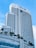 A tall modern hotel building with numerous windows and a sleek architectural design. The hotel name is visible at the top, and there are palm trees adorning the lower levels. The sky is clear with a few white clouds.