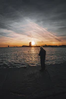 Sunset over a river with a lone angler silhouetted against the glowing sky.