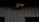 A security camera is mounted on a dark, textured wall. The camera is positioned to monitor an area, possibly outdoor or in a low-light environment.