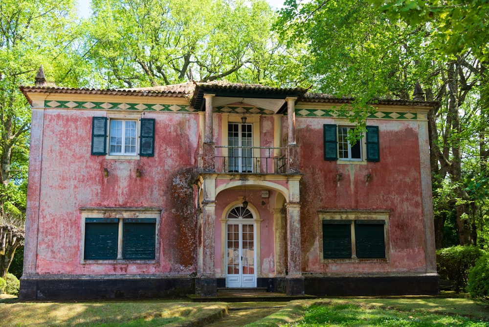 Una casa rosa con persianas verdes y un balcón