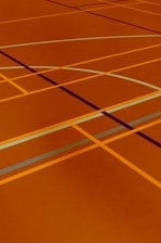 A floor is covered with intersecting lines of varying colors, including orange, blue, and dark brown. These lines form geometric shapes such as rectangles and curves, creating a visually striking pattern.