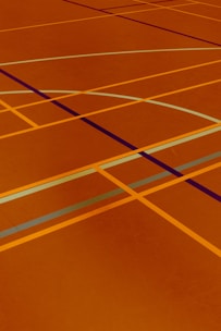 A floor is covered with intersecting lines of varying colors, including orange, blue, and dark brown. These lines form geometric shapes such as rectangles and curves, creating a visually striking pattern.