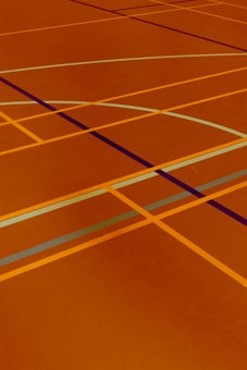 A floor is covered with intersecting lines of varying colors, including orange, blue, and dark brown. These lines form geometric shapes such as rectangles and curves, creating a visually striking pattern.