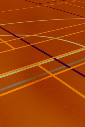 A floor is covered with intersecting lines of varying colors, including orange, blue, and dark brown. These lines form geometric shapes such as rectangles and curves, creating a visually striking pattern.