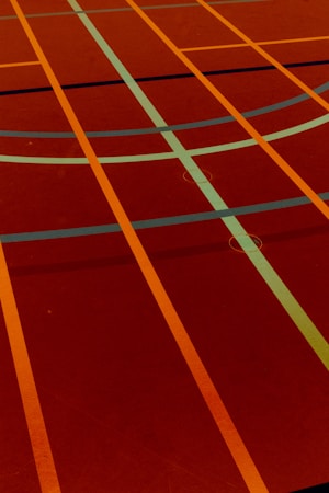 A sports court with intersecting lines in orange and blue, creating geometric patterns on a reddish-brown surface.
