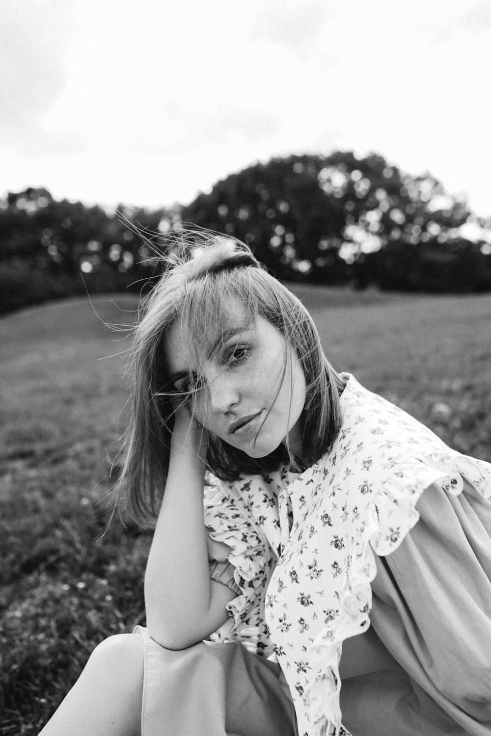 a young girl sitting in a field with her hands on her head