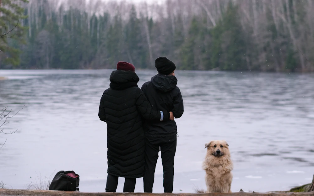 Dos personas con su perro contemplando un lago