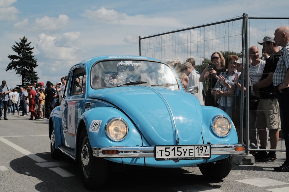 a blue vw bug driving past a crowd of people