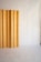 A minimalist interior featuring a vertical wooden panel against a smooth, light-colored backdrop. The panel displays a natural wood grain pattern and is positioned to one side, creating a subtle contrast with the plain surroundings.