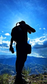 Sunrise view with a hiker silhouetted carrying SummitGearW gear, standing on a ridge overlooking valleys.