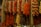 Multiple strands of dried vegetables and herbs, including red peppers, hung from the ceiling in a market setting. The arrangement appears vibrant and rustic, creating a display of texture and color.