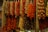Multiple strands of dried vegetables and herbs, including red peppers, hung from the ceiling in a market setting. The arrangement appears vibrant and rustic, creating a display of texture and color.