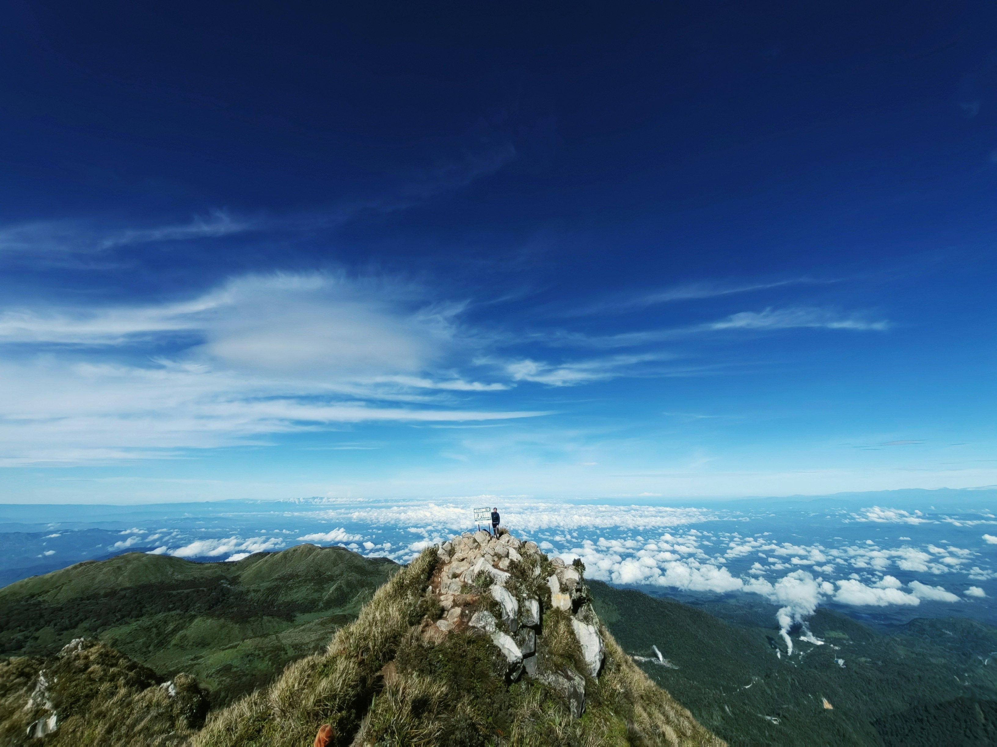 Person standing at mountain summit at sunrise, vast landscape below, bright triumphant atmosphere